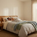 Femme dormant paisiblement dans un lit douillet dans une chambre lumineuse et apaisante. Une plante et une lampe sont visibles.